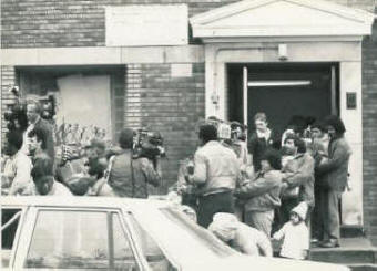 The TV cameras are recording people exiting the building holding Thanksgiving GiveAway grocery bags.